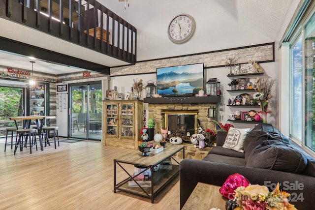 living room with a textured ceiling, a wealth of natural light, light hardwood / wood-style flooring, and a stone fireplace