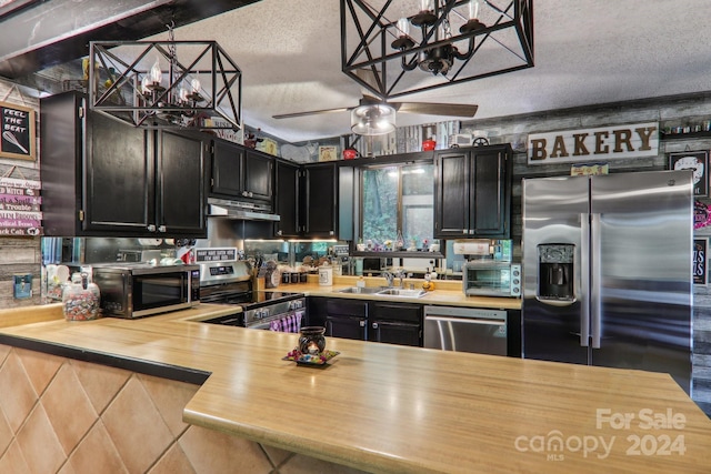 kitchen with a textured ceiling, ceiling fan with notable chandelier, appliances with stainless steel finishes, hanging light fixtures, and sink