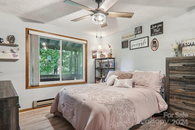 bedroom with a textured ceiling, light hardwood / wood-style flooring, ceiling fan, and a baseboard heating unit