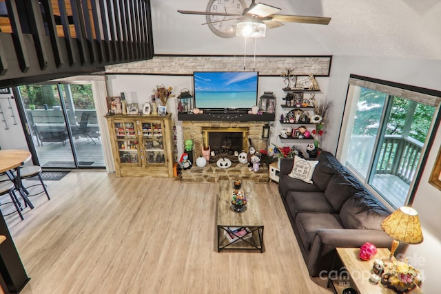 living room with ceiling fan, wood-type flooring, and a stone fireplace