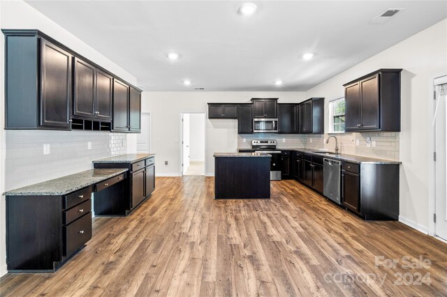 kitchen featuring appliances with stainless steel finishes, light stone counters, sink, wood-type flooring, and a kitchen island