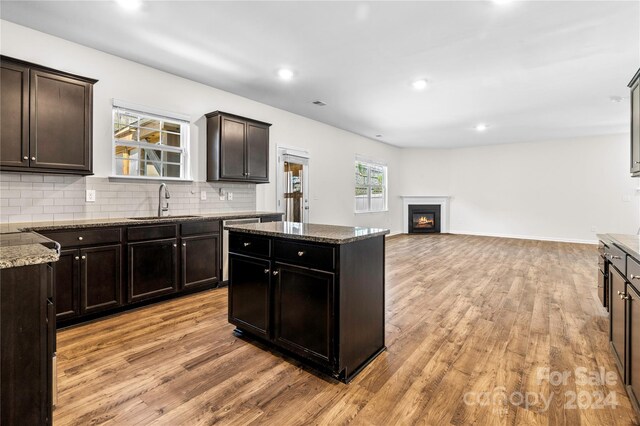 kitchen featuring backsplash, a center island, light wood-type flooring, stone countertops, and sink