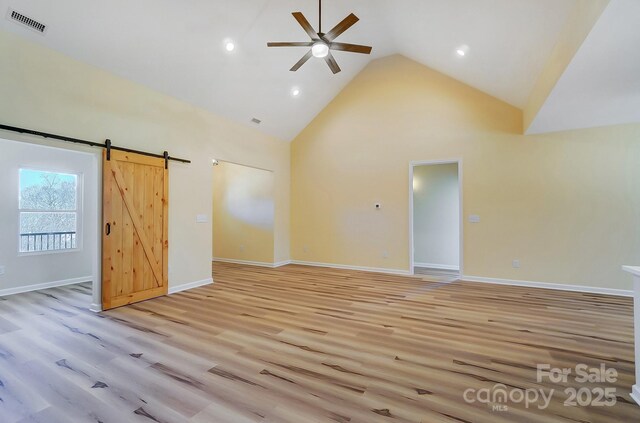 interior space with baseboards, visible vents, high vaulted ceiling, light wood-style flooring, and a barn door