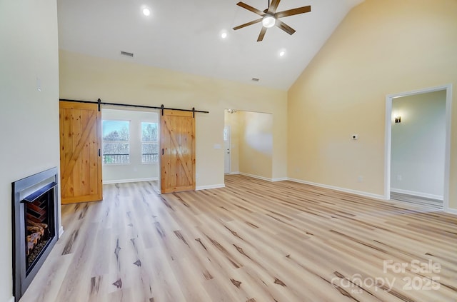 unfurnished living room featuring visible vents, high vaulted ceiling, a barn door, light wood finished floors, and baseboards