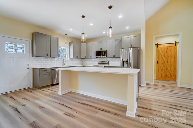 kitchen with decorative backsplash, a barn door, gray cabinets, and appliances with stainless steel finishes