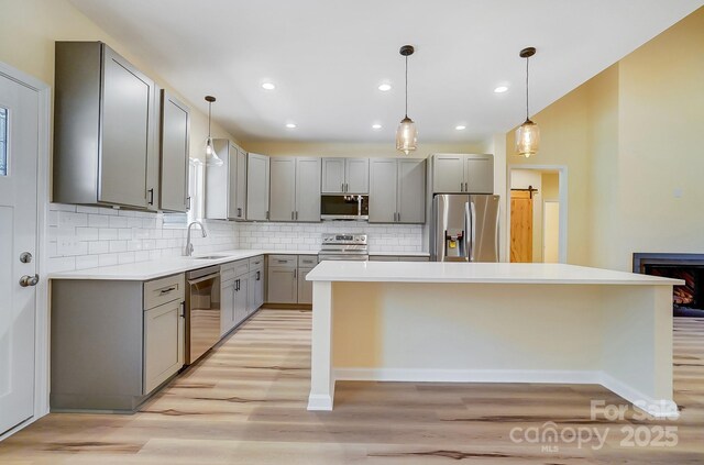 kitchen with light wood-style flooring, gray cabinets, a sink, a center island, and stainless steel appliances