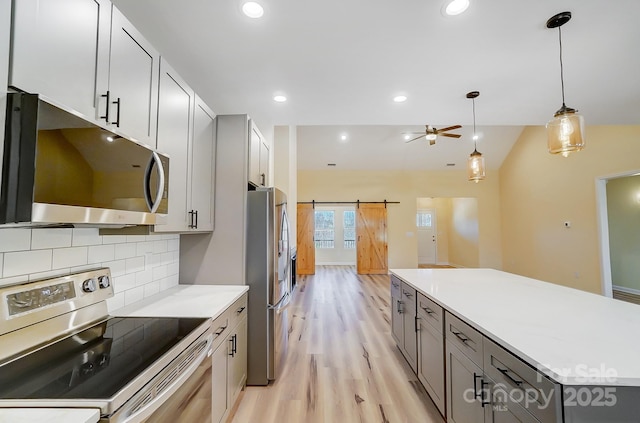 kitchen featuring gray cabinets, appliances with stainless steel finishes, a barn door, light wood-type flooring, and backsplash