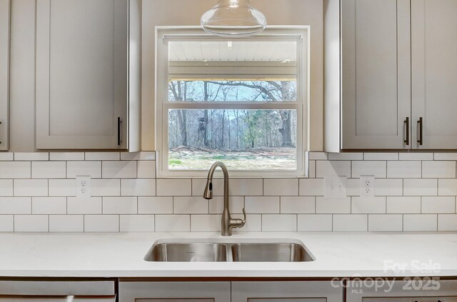 kitchen featuring light countertops, gray cabinets, backsplash, and a sink