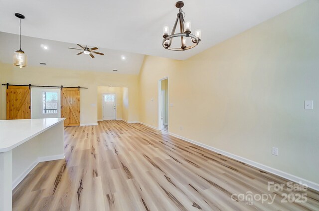 interior space with baseboards, lofted ceiling, a barn door, ceiling fan with notable chandelier, and light wood-type flooring