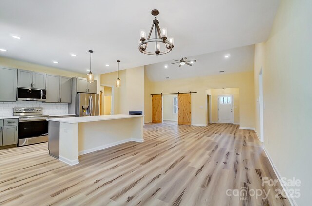 kitchen featuring gray cabinetry, a barn door, appliances with stainless steel finishes, light wood finished floors, and light countertops