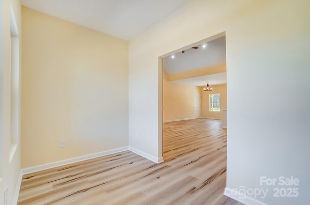 empty room featuring baseboards, an inviting chandelier, and wood finished floors