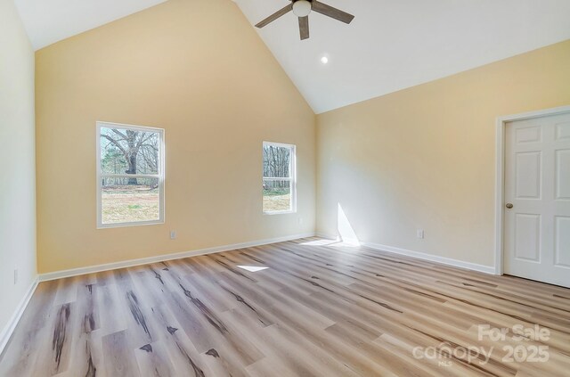 spare room with baseboards, ceiling fan, high vaulted ceiling, and light wood-style floors