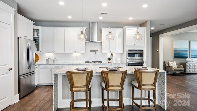 kitchen featuring hanging light fixtures, light stone countertops, stainless steel appliances, dark hardwood / wood-style flooring, and wall chimney range hood