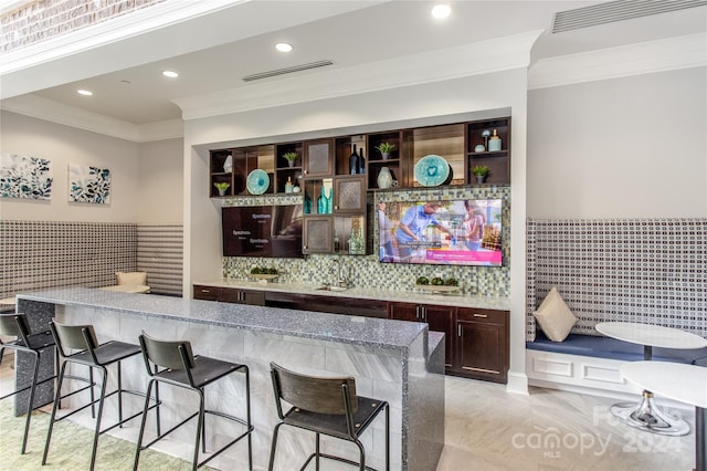 bar featuring tile walls, light stone countertops, dark brown cabinetry, and ornamental molding