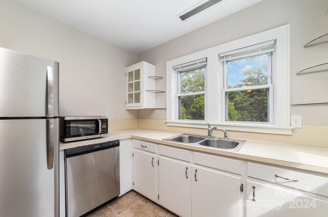 kitchen featuring sink, light tile patterned floors, appliances with stainless steel finishes, and white cabinetry