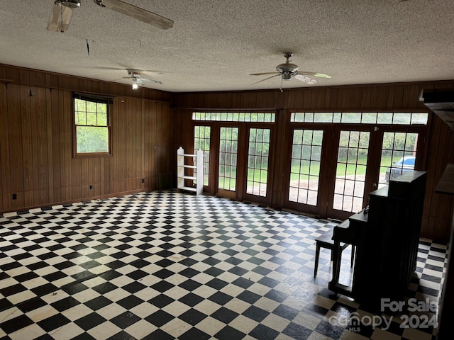 unfurnished living room with wooden walls, ceiling fan, and a textured ceiling