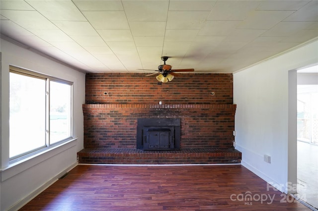 unfurnished living room with a wood stove, ceiling fan, wood-type flooring, and brick wall