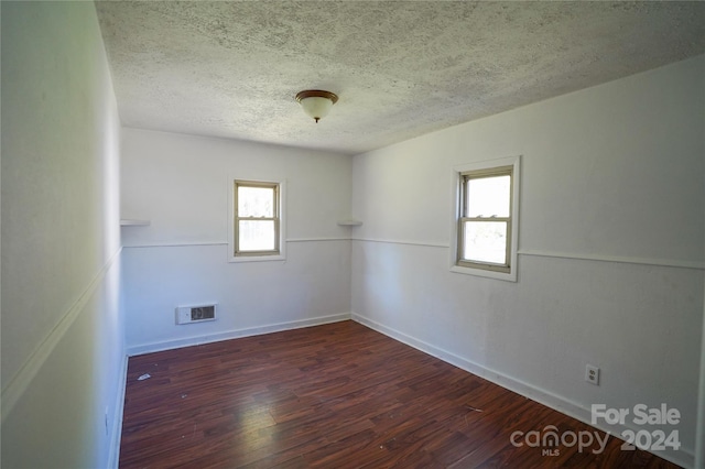 spare room featuring a textured ceiling, plenty of natural light, and dark wood-type flooring