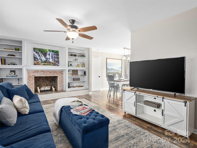 living room with built in shelves, ceiling fan, dark hardwood / wood-style flooring, and a brick fireplace