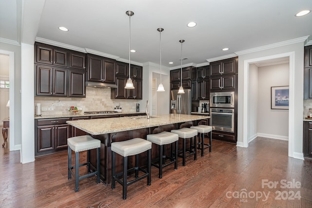 kitchen with an island with sink, decorative light fixtures, dark wood-type flooring, appliances with stainless steel finishes, and a kitchen bar