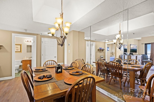 dining space featuring a textured ceiling, light hardwood / wood-style flooring, a tray ceiling, and a chandelier