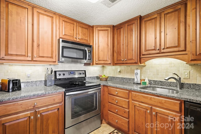 kitchen featuring dark stone countertops, backsplash, appliances with stainless steel finishes, sink, and a textured ceiling