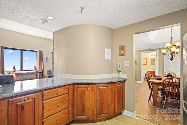 kitchen featuring pendant lighting, a notable chandelier, a textured ceiling, light hardwood / wood-style flooring, and light stone counters