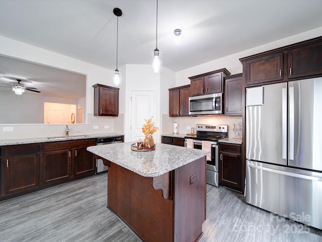 kitchen with ceiling fan, hanging light fixtures, light hardwood / wood-style floors, a breakfast bar area, and appliances with stainless steel finishes