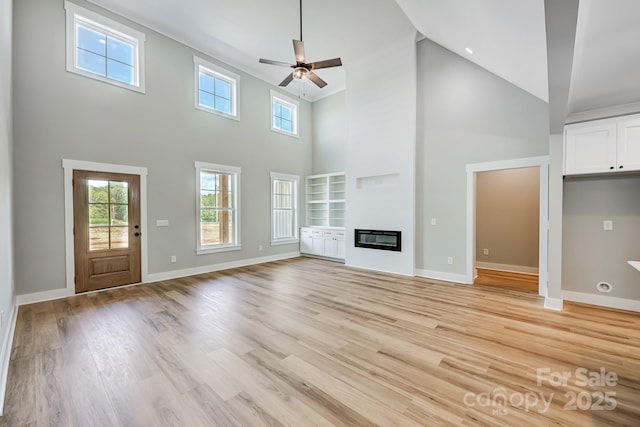 unfurnished living room featuring ceiling fan, light wood-type flooring, and a high ceiling