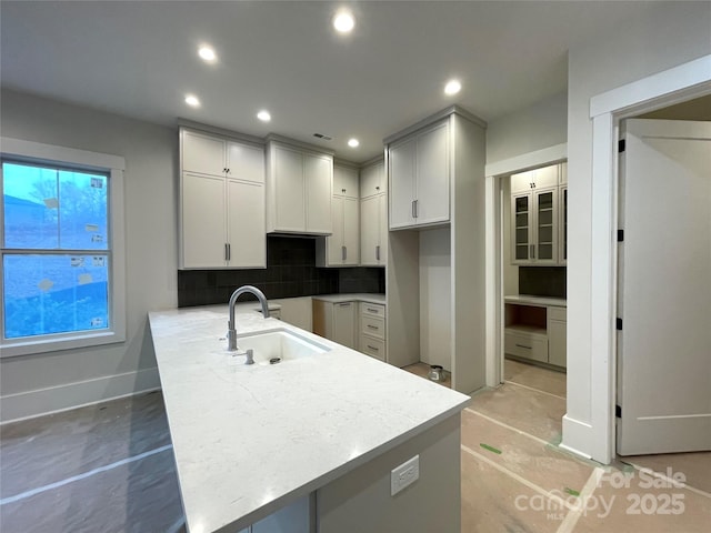 kitchen with sink, decorative backsplash, light stone countertops, and kitchen peninsula