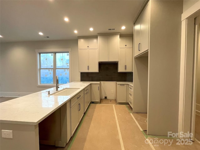 kitchen with sink, white cabinets, decorative backsplash, kitchen peninsula, and light stone countertops