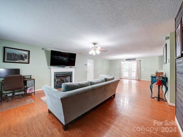 living room with ceiling fan, a textured ceiling, light hardwood / wood-style flooring, and a fireplace