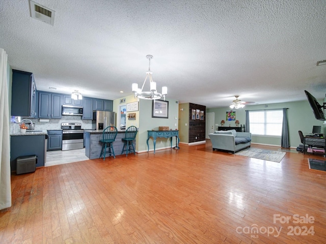 kitchen with a textured ceiling, sink, ceiling fan with notable chandelier, light hardwood / wood-style flooring, and stainless steel appliances