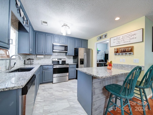 kitchen with appliances with stainless steel finishes, a kitchen breakfast bar, kitchen peninsula, light stone countertops, and sink