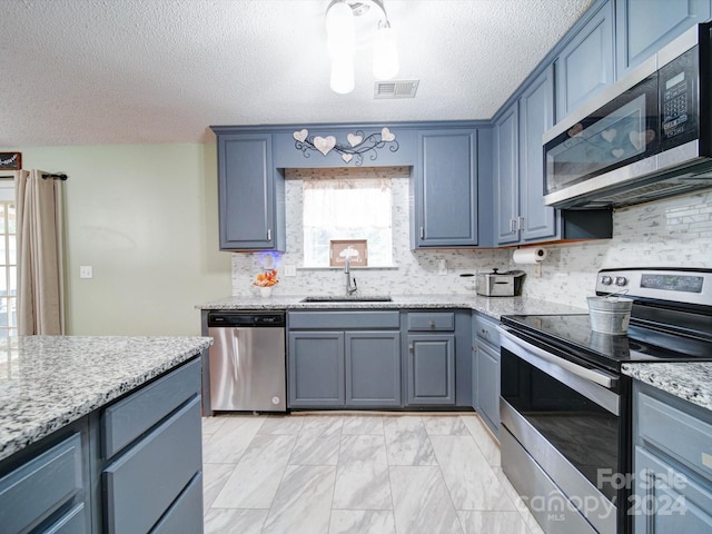 kitchen featuring light stone counters, a textured ceiling, sink, decorative backsplash, and appliances with stainless steel finishes