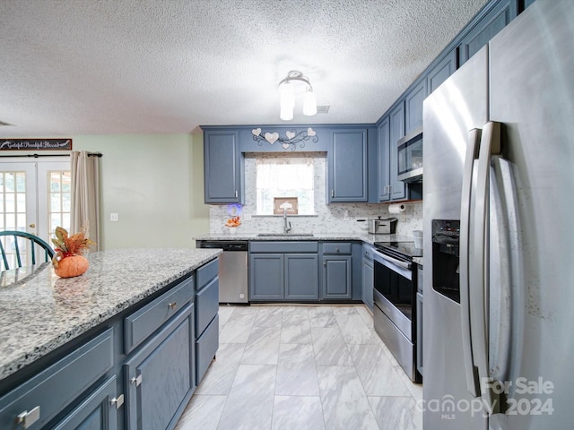 kitchen with light stone countertops, stainless steel appliances, sink, and a healthy amount of sunlight