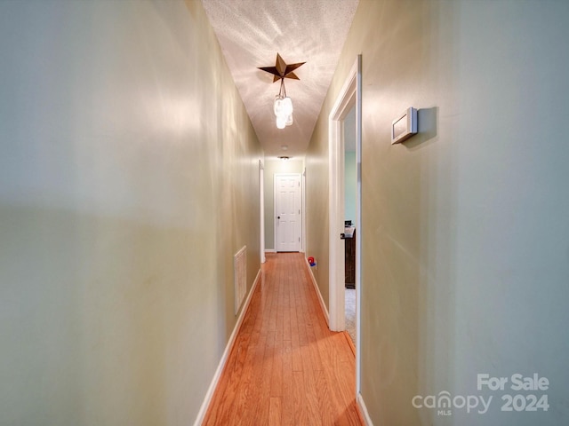 corridor with a textured ceiling and light hardwood / wood-style floors