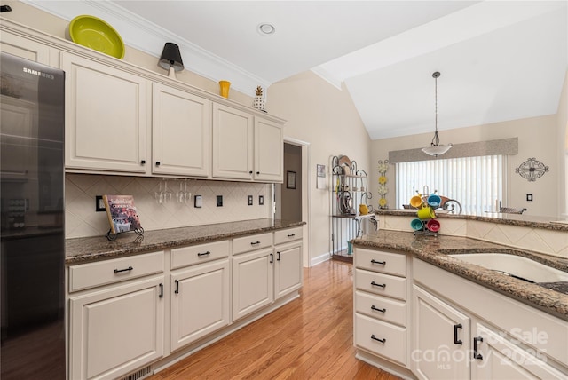 kitchen with decorative light fixtures, backsplash, lofted ceiling, and dark stone counters