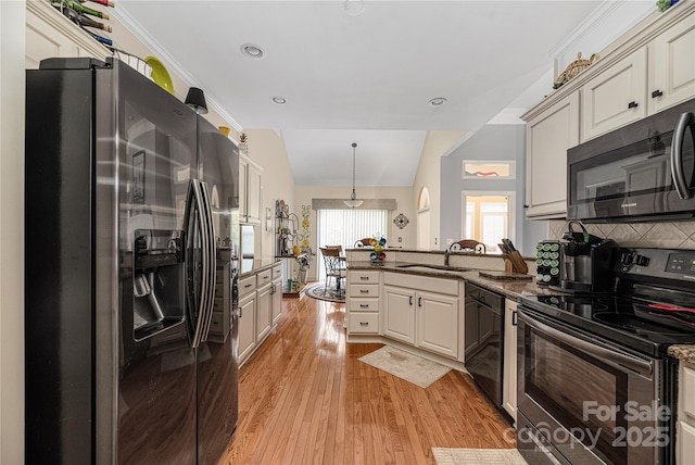 kitchen featuring pendant lighting, appliances with stainless steel finishes, sink, vaulted ceiling, and light hardwood / wood-style flooring