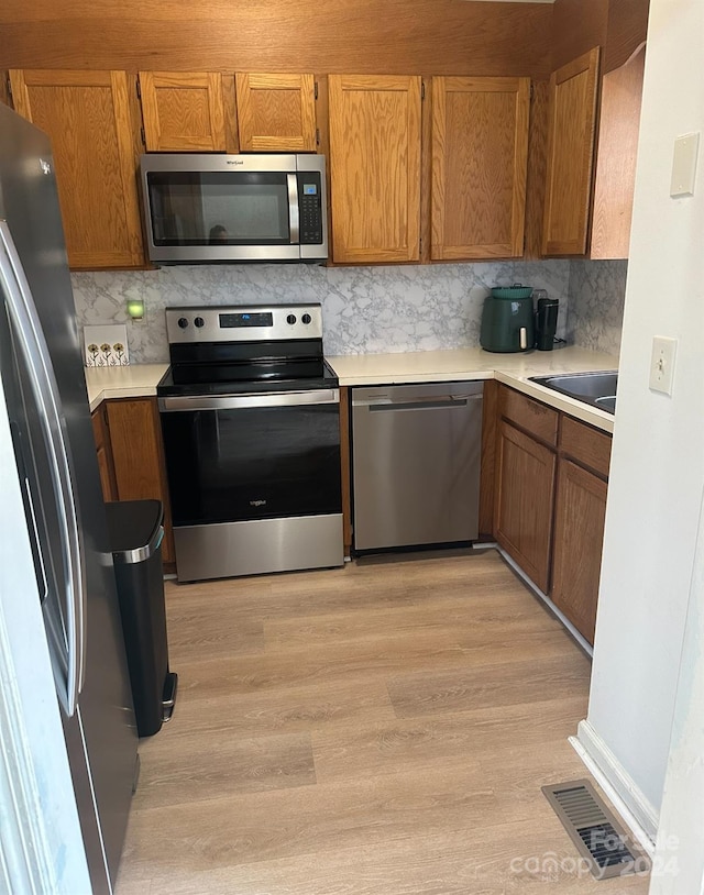 kitchen featuring stainless steel appliances, light wood-type flooring, sink, and tasteful backsplash