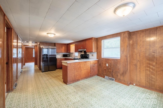 kitchen with stainless steel fridge, black stove, kitchen peninsula, and wooden walls