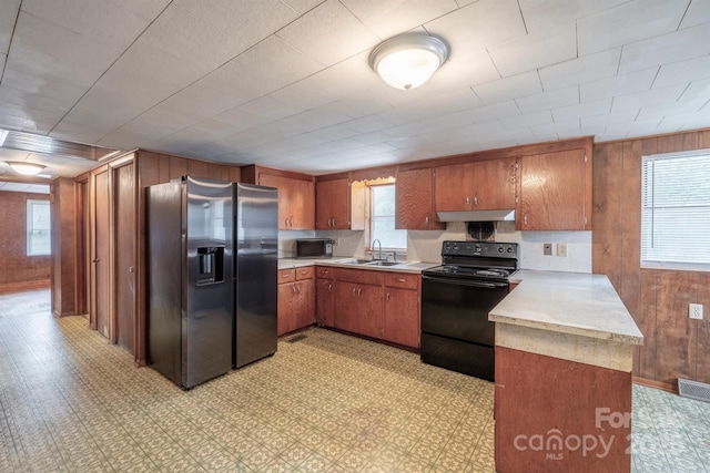 kitchen with kitchen peninsula, wooden walls, sink, and black appliances