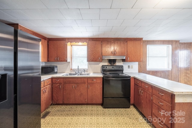 kitchen with brown cabinets, under cabinet range hood, light countertops, black appliances, and a sink