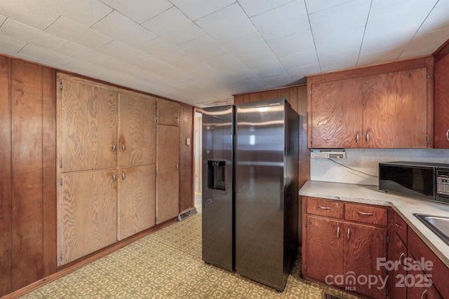 kitchen featuring stainless steel fridge with ice dispenser, wooden walls, and sink