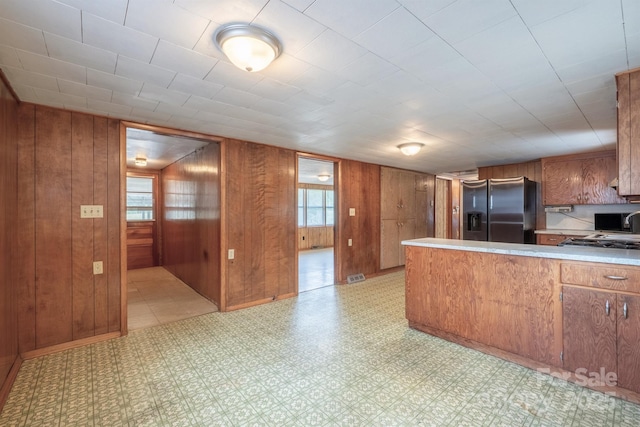 kitchen with kitchen peninsula, stainless steel fridge with ice dispenser, and wooden walls