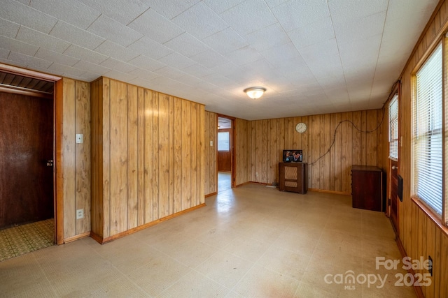 spare room featuring a wealth of natural light, baseboards, wooden walls, and light floors