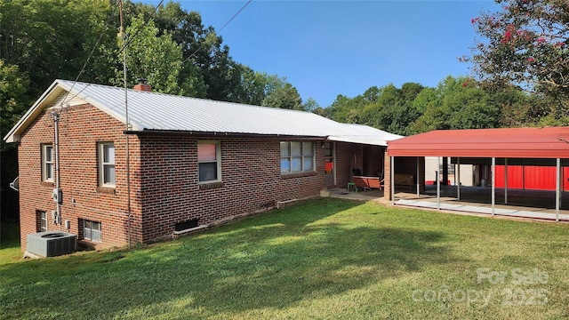 rear view of house featuring central AC, metal roof, a lawn, and brick siding