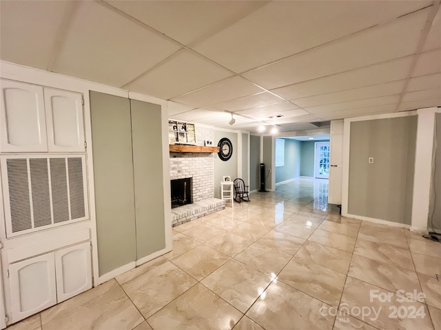 interior space featuring a paneled ceiling, a brick fireplace, and light tile patterned flooring