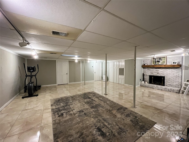 basement featuring light tile patterned floors, a brick fireplace, and a paneled ceiling