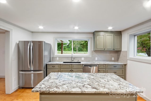 kitchen featuring light wood finished floors, tasteful backsplash, appliances with stainless steel finishes, light stone countertops, and a sink